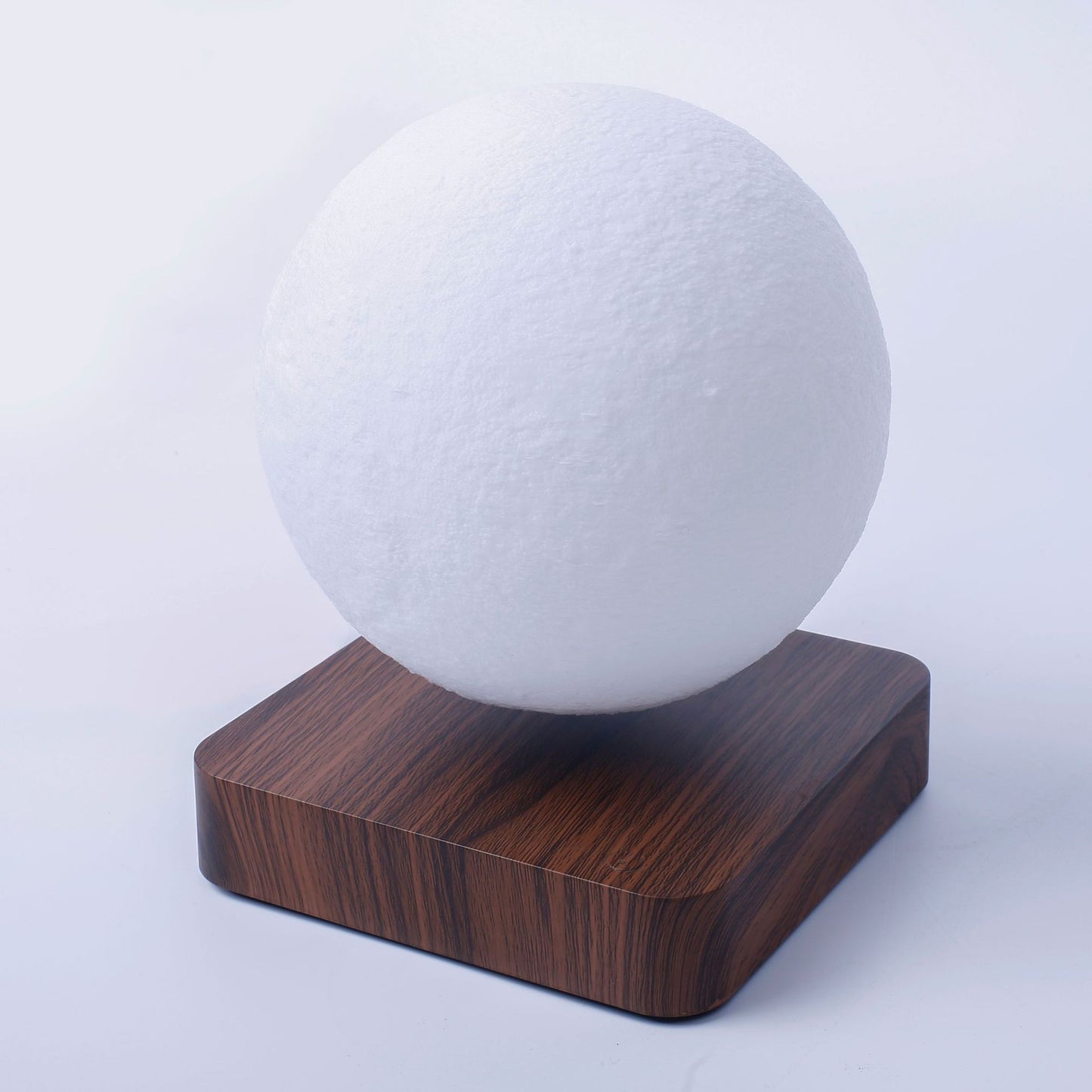 White spherical object on a wooden base against a light gray background