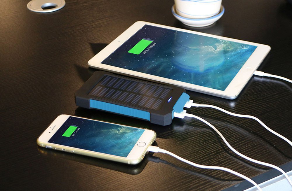 Solar power bank charging a smartphone and tablet on a dark surface